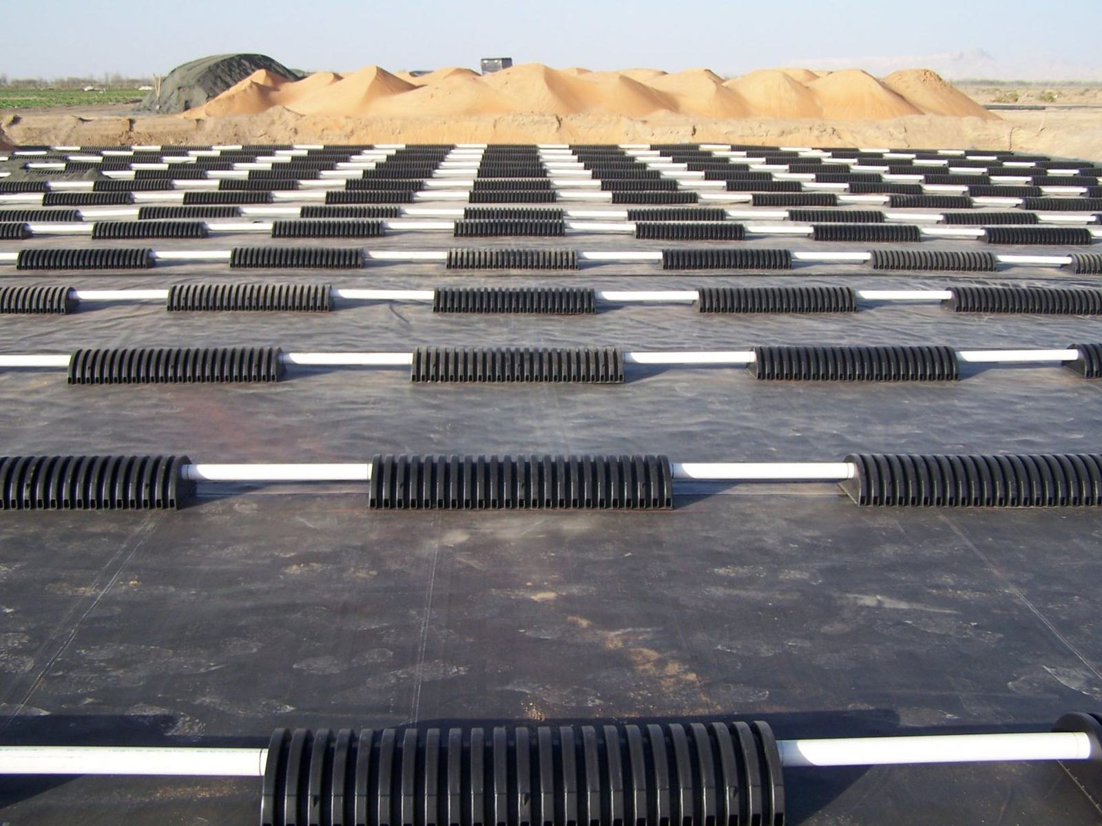 A grid of chambers on the liner at a desert farm, dunes behind